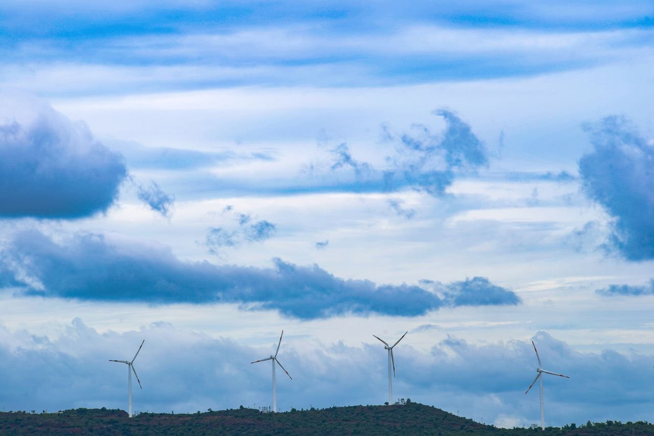 Wind turbines on a hill under a blue sky and scattered clouds, promoting renewable energy.